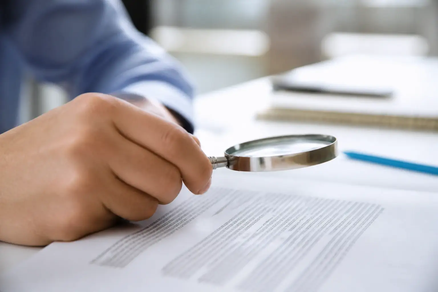 A magnifier held over a single paragraph of a printed page, the rest of the sheet in shadow